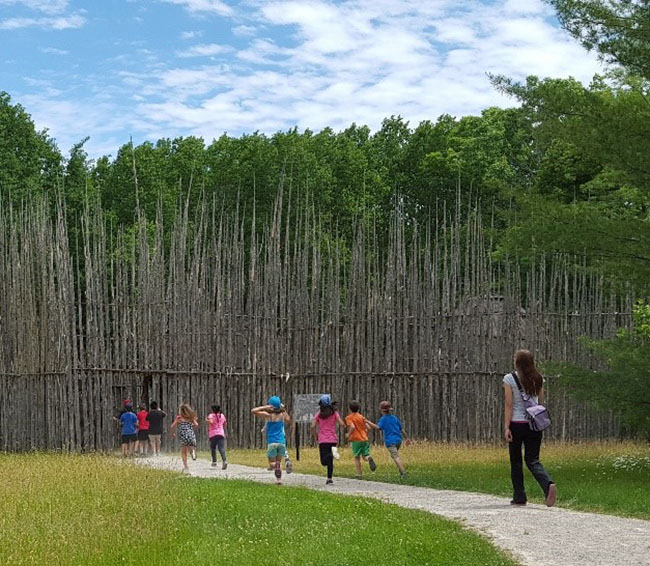 kids running towards Ska-Nah-Doht Village palisade