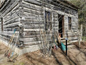 Heritage Log Cabin with rakes and gardening tools leaning against the wall.
