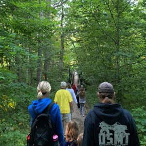 Activity participants walk towards a suspension bridge on a sunny summer morning.