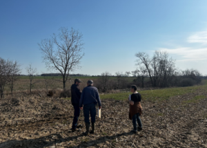Three people gather in a farm field.